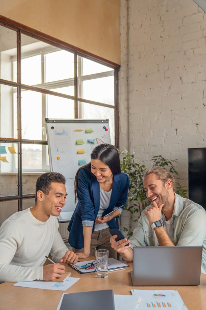 Vertical shot of multiracial business people with laptop and smartphone having meeting in office.