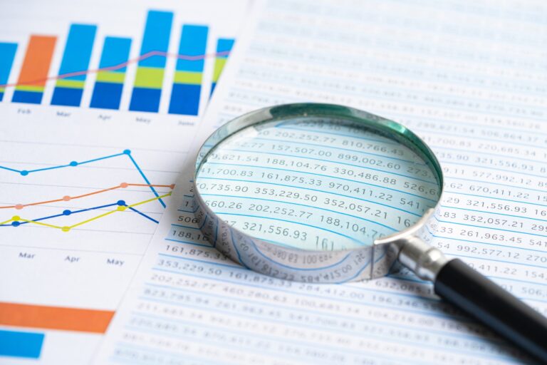 Magnifying glass on chart graph spreadsheet paper.