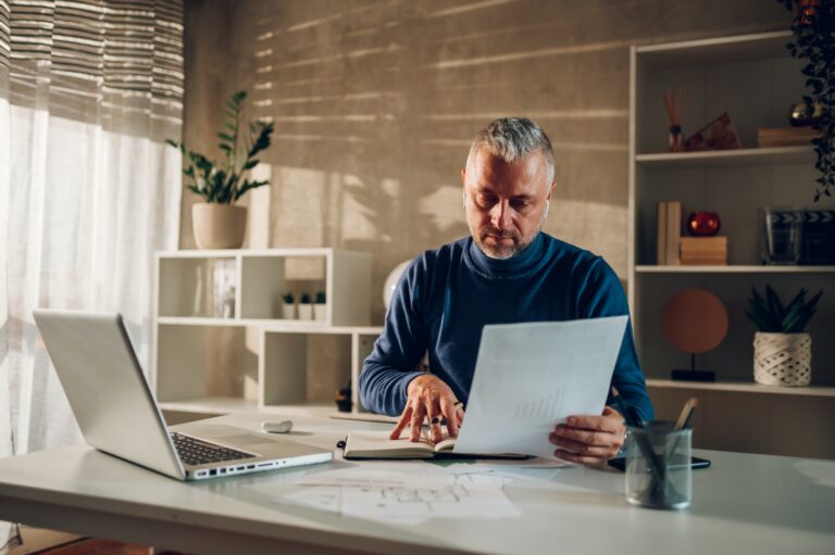 Middle aged man working in a home office and using laptop and paper documents